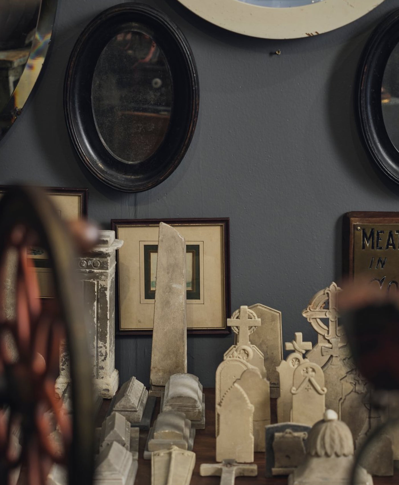 Vintage-style room with framed pictures, mirrors, and decorative tombstones on a graphite grey wall.