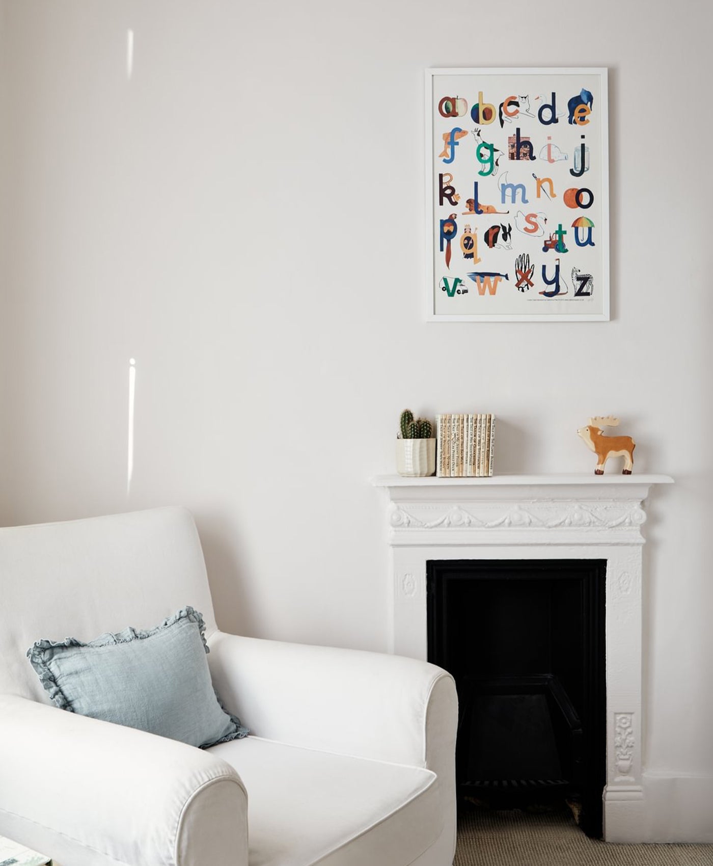 Children's room in pale neutral colour with a white armchair, fireplace, and alphabet poster on the wall.
