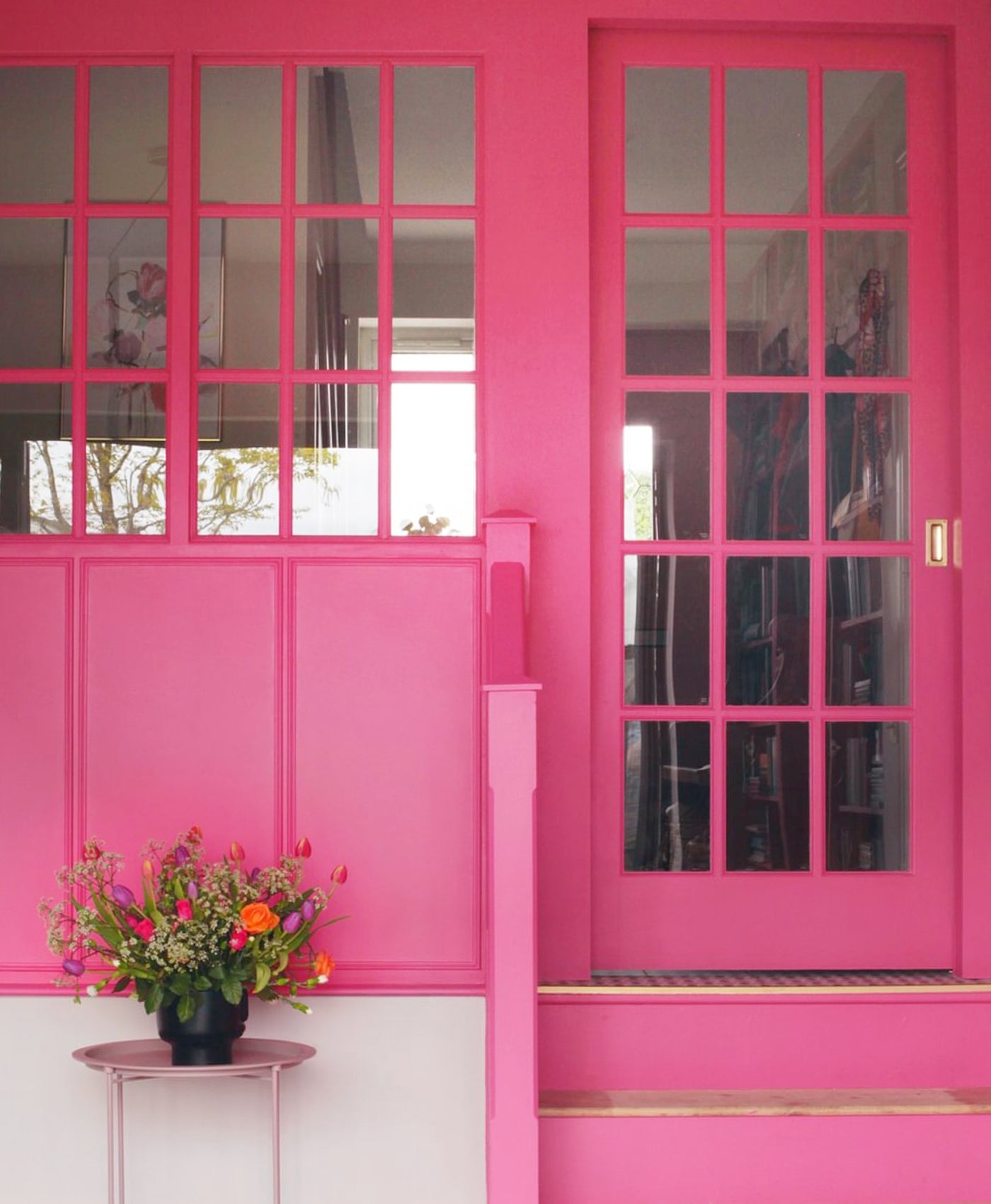 Bright pink door with glass panels and a small table with flowers in front.