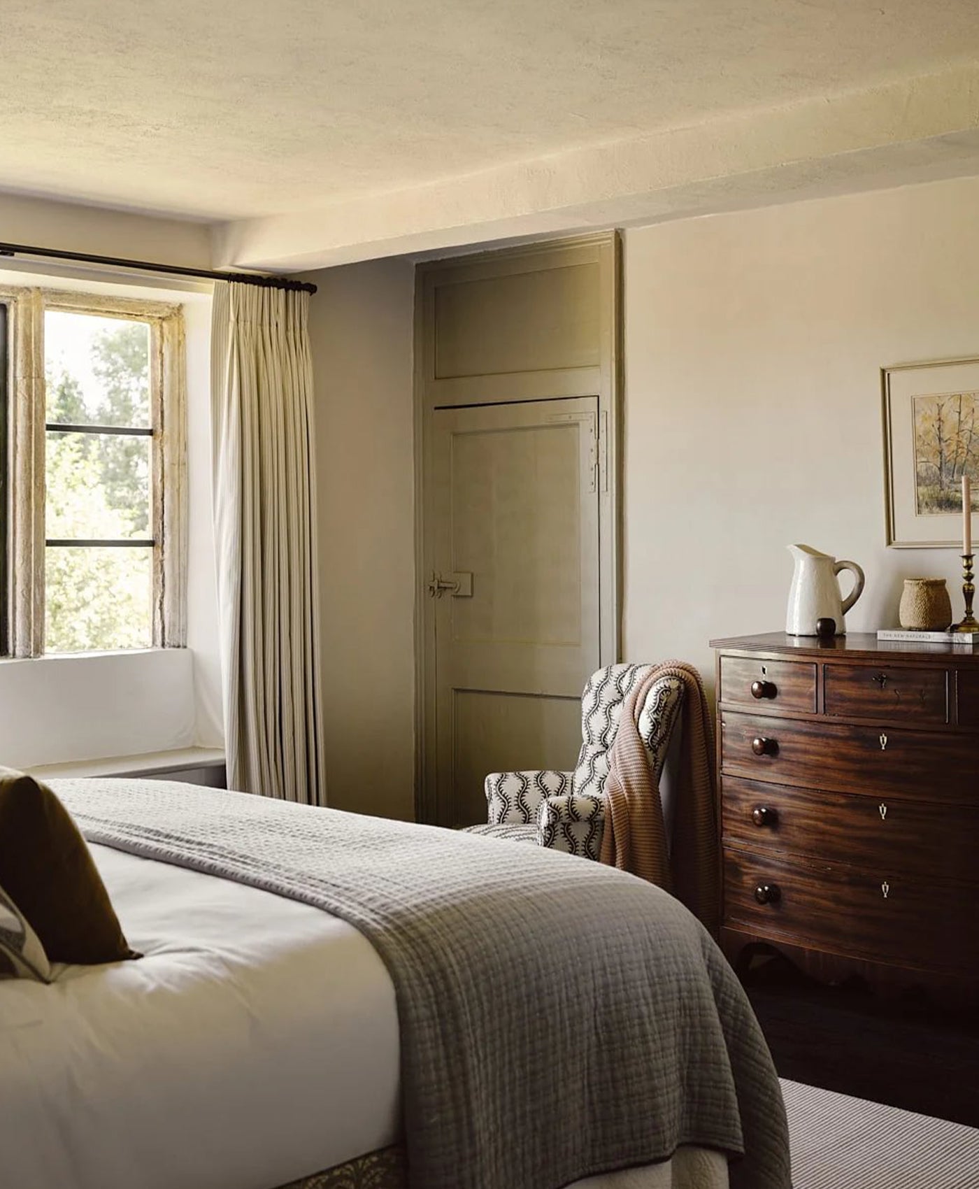Cosy bedroom in warm stone paint with a bed, chair, and dresser.
