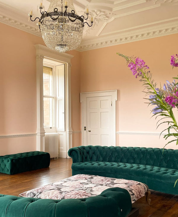Luxurious pale pink living room with green velvet sofa, chandelier, and floral arrangement.