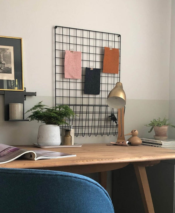 Home office setup with a wooden desk, chair, lamp, and wall-mounted grid organiser, room painted in pale neutral colour