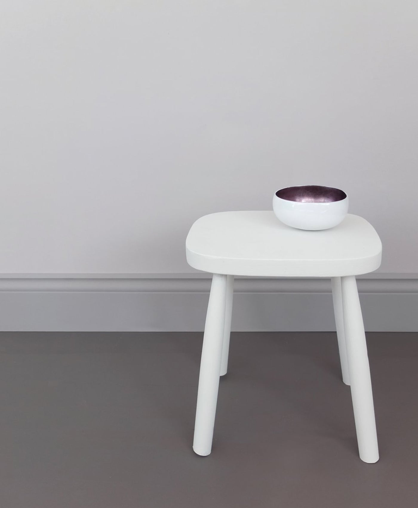 White stool with a small bowl on a grey floor against a light gray wall