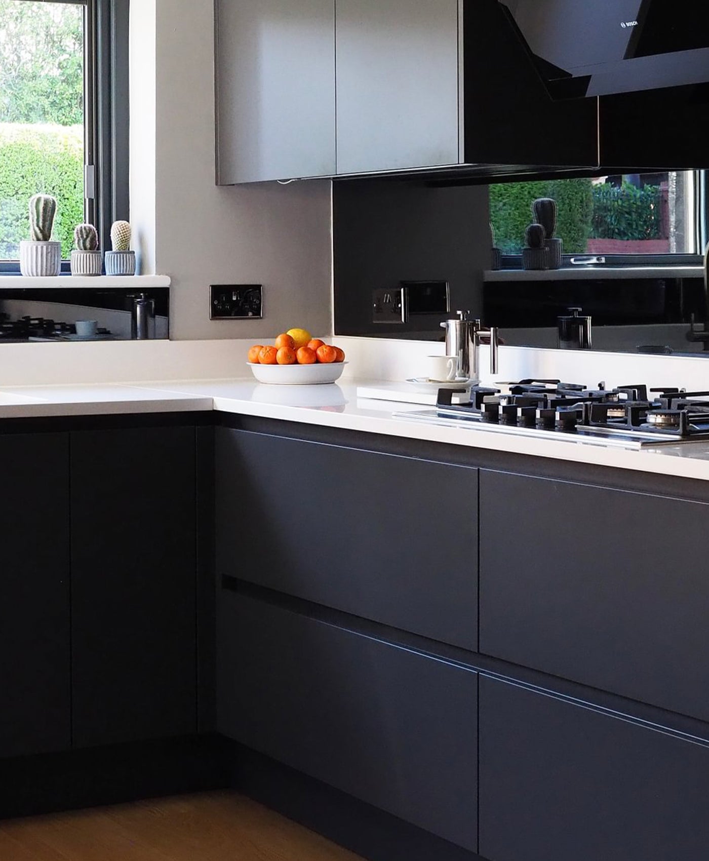 Modern kitchen with black cabinets, white countertops, and a bowl of oranges.