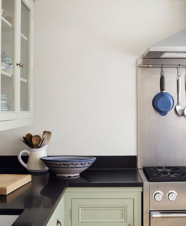 Snow white modern kitchen with black countertops, green cabinets, and stainless steel appliances.