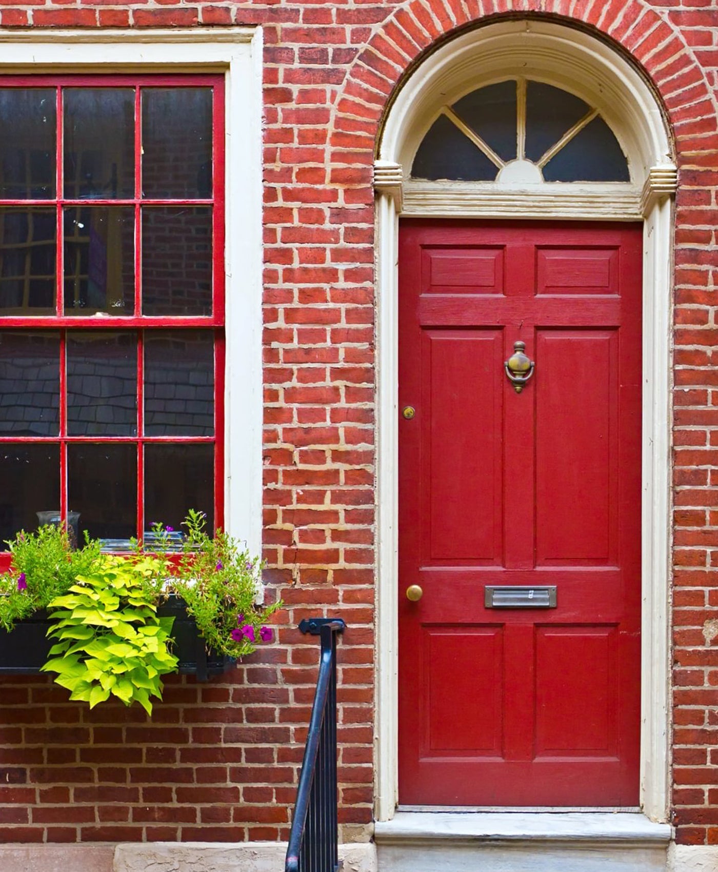 Red door on a brick building with a window box of flowers.