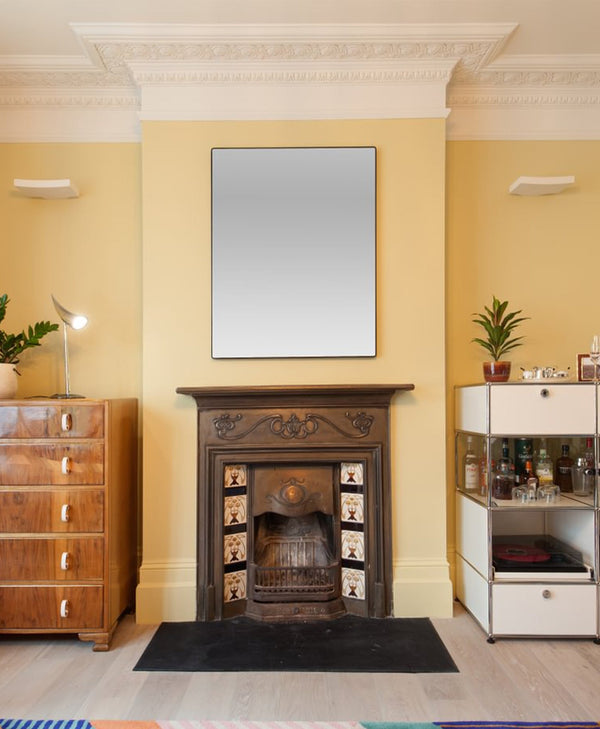 Traditional fireplace with wooden mantel in a room with butter yellow walls, a mirror, and furniture.