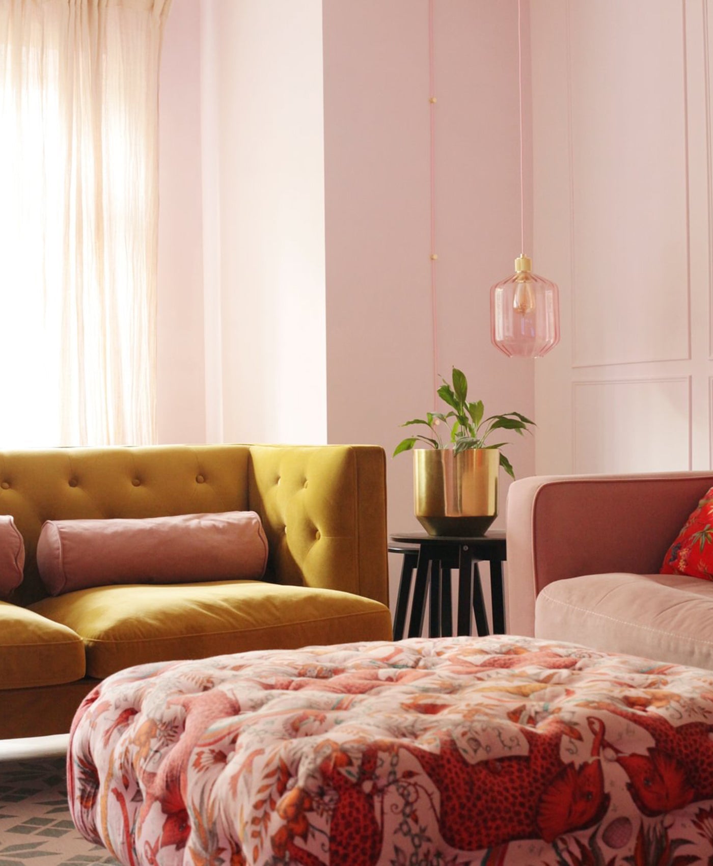 Living room with a yellow sofa, pink and orange patterned ottoman, and blush pink walls.
