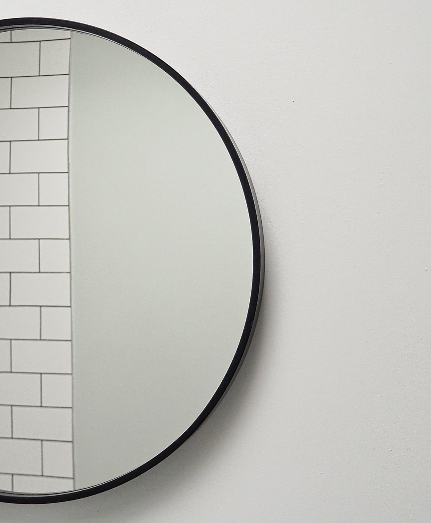 Round mirror with black frame on a light grey wall