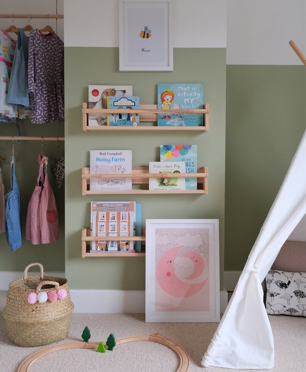 Olive green children's room with shelves displaying books and toys, a pink wall art, and a white teepee.