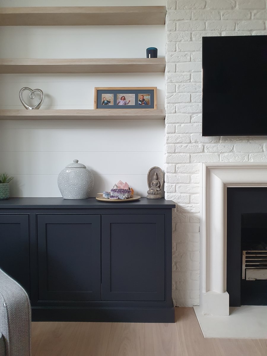 Nest living room with black cabinet, light wood shelves, and white brick fireplace.